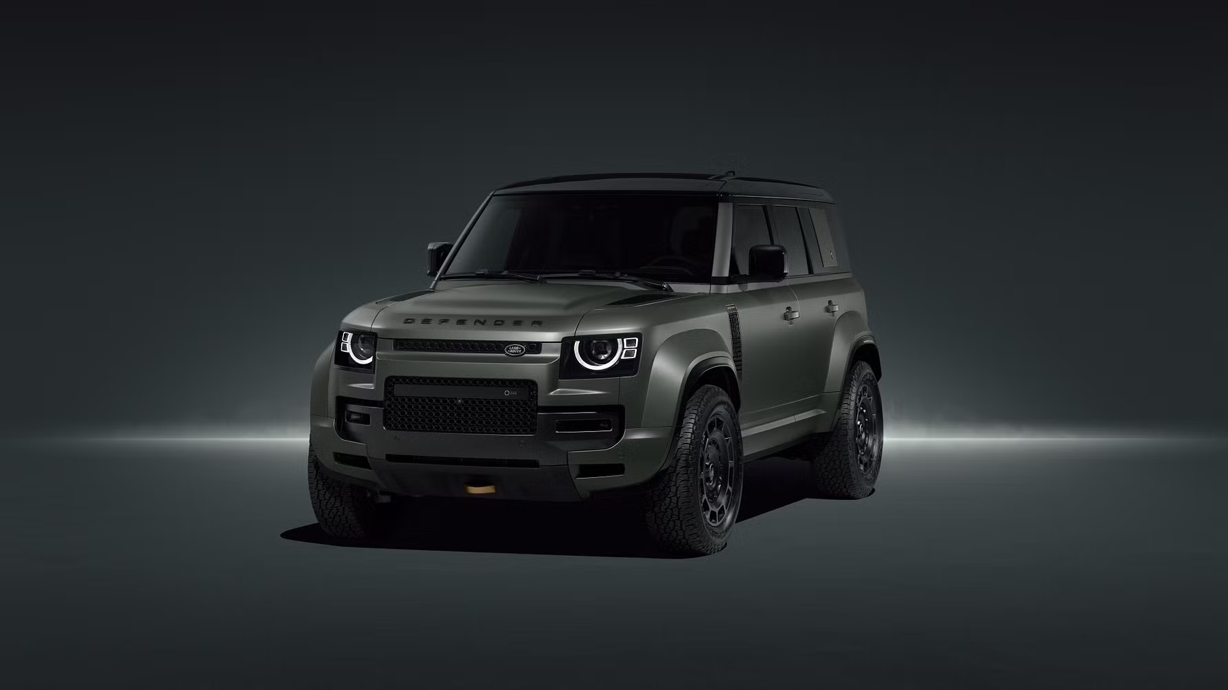 A dark green Land Rover Defender OCTA with rugged tires displayed under minimal lighting in a studio setting.