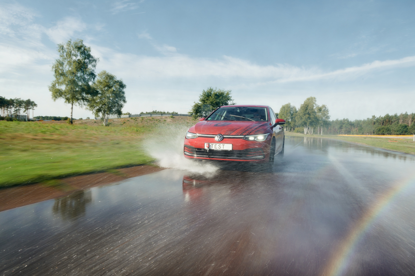 Red Volkswagen splashing through water during the ADAC 2022 summer tire test at Contidrom, showcasing wet road performance.
