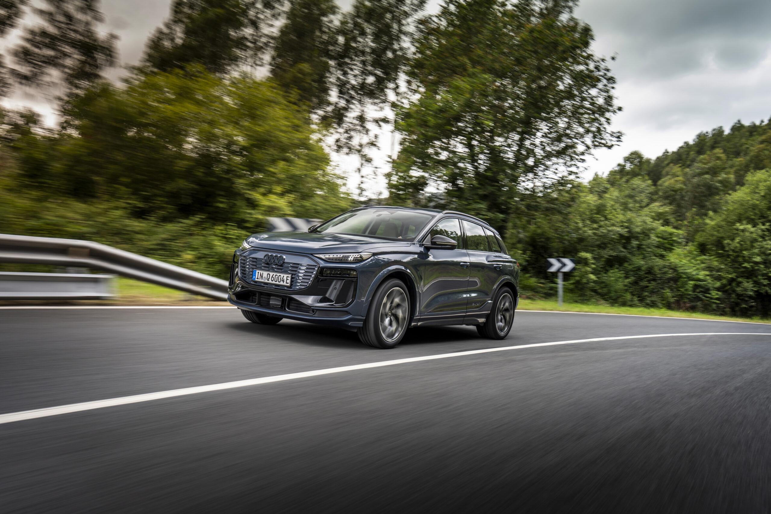 Audi Q6 e-tron SUV driving along a curved road surrounded by greenery, highlighting its sleek design and electric capabilities.