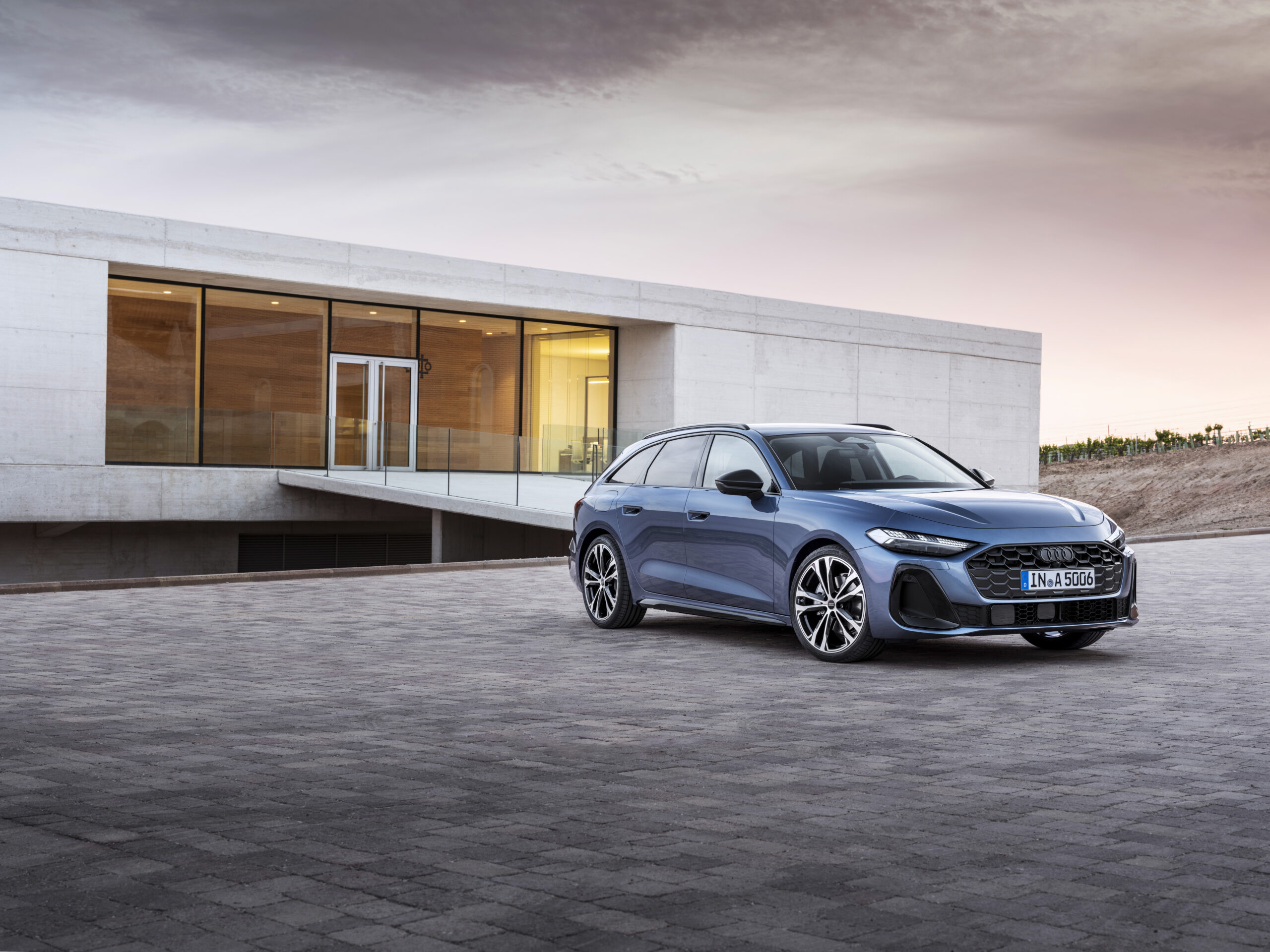 Blue Audi A5 parked in front of a sleek, modern building with large windows, highlighting the car's elegant design.