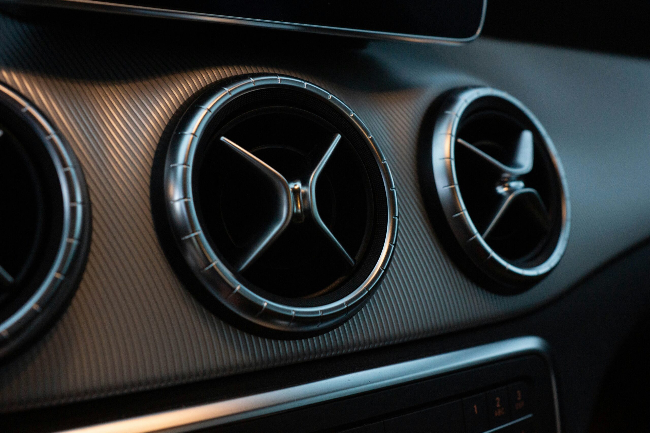 Close-up of three circular car air vents with a sleek metallic finish and modern design on the dashboard.