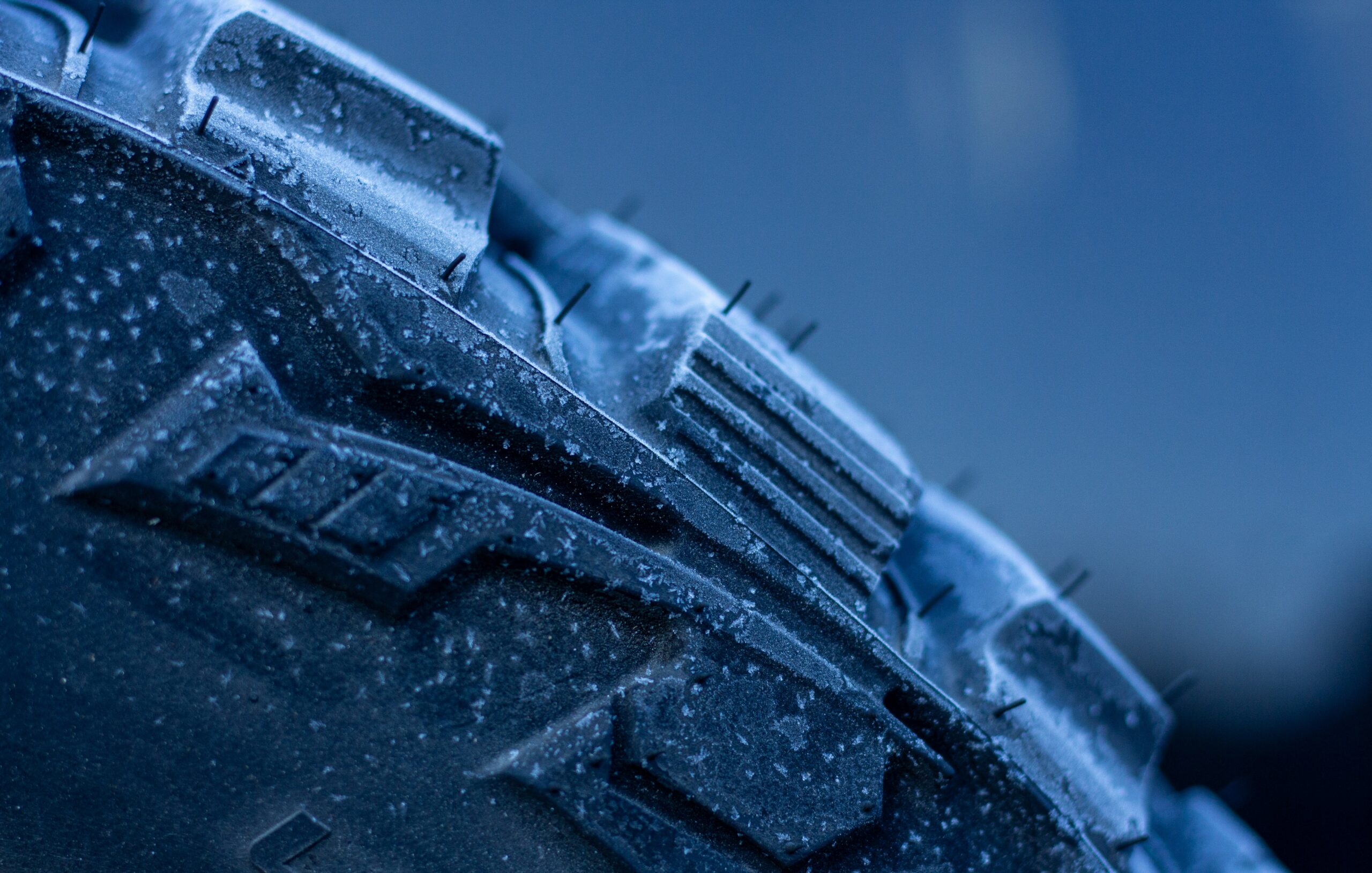 Close-up of a frosty tire tread, showcasing rugged patterns and small spikes for enhanced traction in icy conditions.
